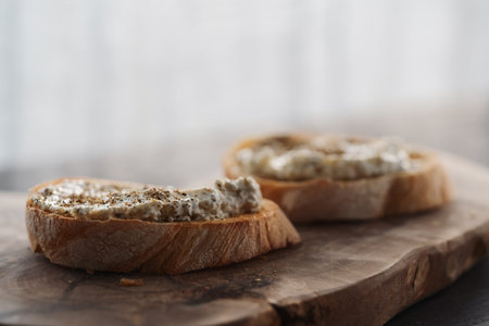 Ciabatta slices with cream cheese and herbs on olive wood board