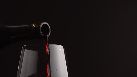 pour red wine into wineglass on black background