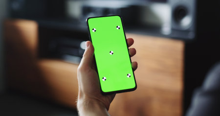 man holding smartphone with green screen near tv standの写真素材