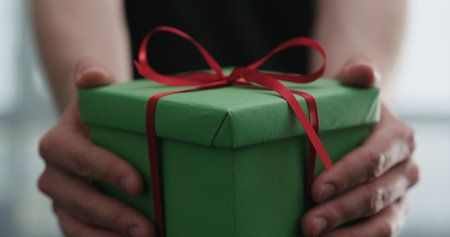 young man shows green paper gift box with red ribbonの写真素材