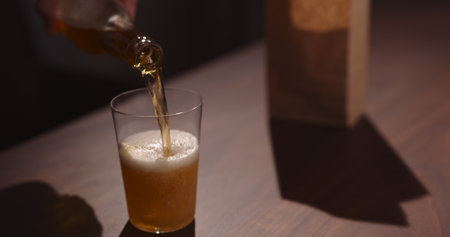 Man pour amber color fizzy drink in tumbler glass with bag of potato chips on backgroundの写真素材