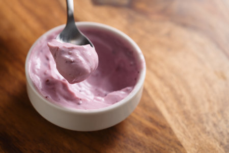 eating blueberry yogurt from white bowl on wood tableの写真素材