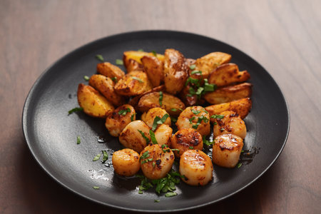 roasted scallops with baked potatoes wedges on a black plate on walnut wood backgroundの写真素材