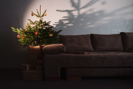 Small christmas tree with natural decorations and presents indoor near couch with warm lightの写真素材