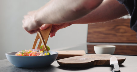 Man mixing greek salad in blue bowl with wood serversの写真素材