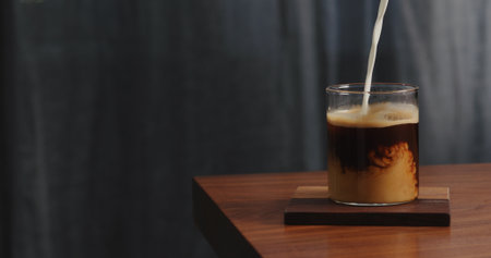 cream pour into coffee in glass on walnut tableの写真素材