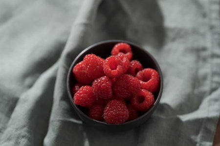 Raspberries in black bowl on linen napkin closeup