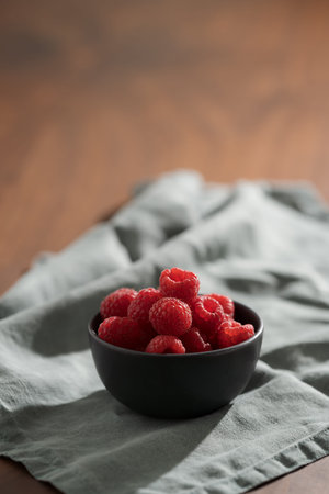 Raspberries in black bowl on linen napkin closeup