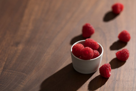 Fresh raspberries in small white bowl on wood table closeup