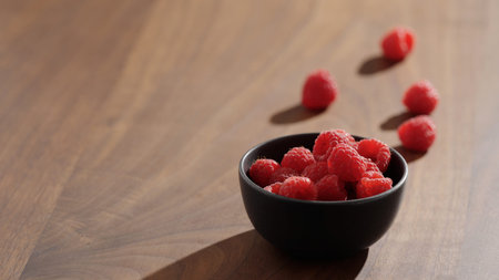 raspberries in black bowl on wood table