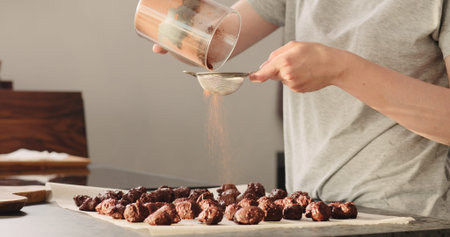 young woman sprinkle cocoa powder on chocolate truffles