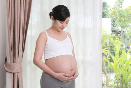 Asian woman pregnant looking at the womb happily at home, (with clipping path)
