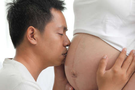 Face of young Asians kiss belly of a pregnant wife happilyの写真素材