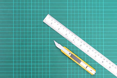 Cutter yellow handle with scratches from use and metal ruler,Placed on the green cutting matの写真素材