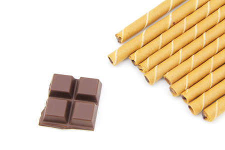 Striped wafer rolls filled with a mixture of chocolate and  square chocolate on a white backgroundの写真素材