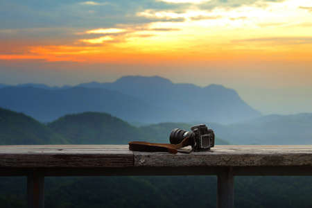 Dslr photo camera is placed on a wooden terrace with a beautiful background of sunrise.の写真素材