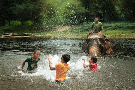 Unidentified youngs mahout enjoying splashing water with elephants in the forest at Kanchanaburi province in Thailand on May 24, 2015,のeditorial素材
