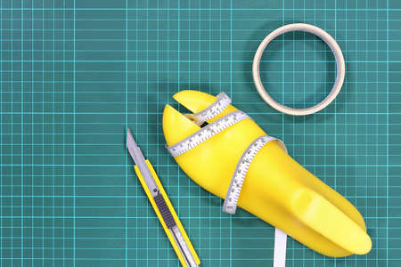 Yellow plastic last shoe and equipment used in shoe design on green grid pattern background (cutting...