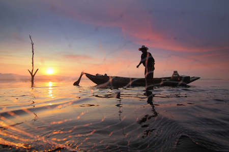 Silhouette of fishermen using nets to catch fish at the Bangpra lake with beautiful scenery of nature during sunrise time. Bang Pra Reservoir at Chonburi province in Thailandの写真素材