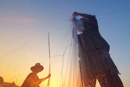 Silhouette of fishermen using nets to catch fish at the Bangpra lake with beautiful scenery of nature during sunrise time. Bang Pra Reservoir at Chonburi province in Thailandの写真素材