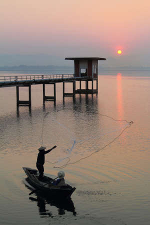 Silhouette of fishermen using nets to catch fish at the Bangpra lake with beautiful scenery of nature during sunrise time. Bang Pra Reservoir at Chonburi province in Thailandの写真素材