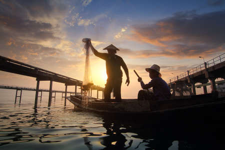 Silhouette of fishermen using nets to catch fish at the Bangpra lake with beautiful scenery of nature during sunrise time. Bang Pra Reservoir at Chonburi province in Thailandの写真素材