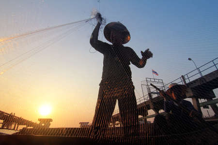 Silhouette of fishermen using nets to catch fish at the Bangpra lake with beautiful scenery of nature during sunrise time. Bang Pra Reservoir at Chonburi province in Thailandの写真素材
