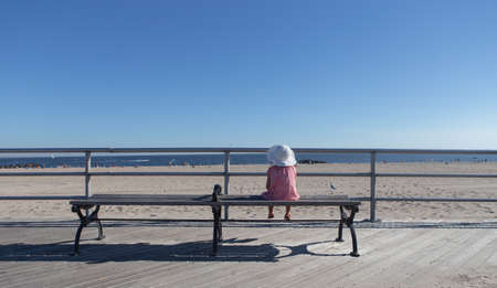 Little girl sitting on the bench looking at the beach. Photographed in Coney Island, Brooklyn NY, USA in September 2015.の写真素材