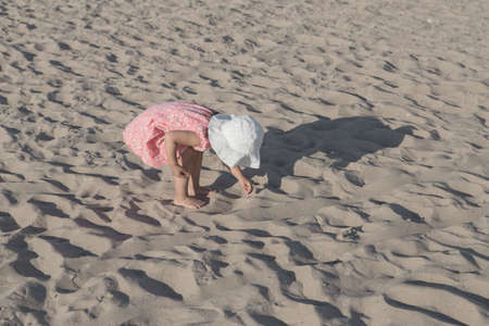 Little girl in pink dress playing with sand on the beach in Coney Island, Brooklyn, NY, USA. Photographed in September 2015.の写真素材