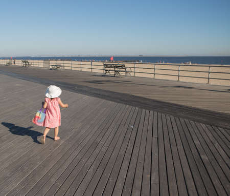 Little girl walking on the boardwalk in a sunny day. Photographed in Coney Island, Brooklyn, NY, USA in September 2015.の写真素材