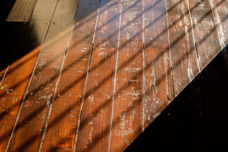 sunlight from window with bars falling on wooden floor, wooden wall background in a morning light with shadows from a window frameの写真素材