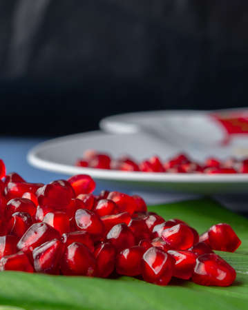 Pomegranate fruit seeds stacked together on a green leaf and a white plateの写真素材