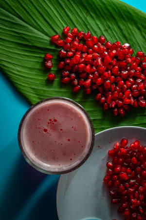 Pomegranate fruit seeds stacked together on a green leaf and a white plate along with its juiceの写真素材