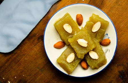 Indian homemade dessert wheat halwa garnished with badam on a colorful background