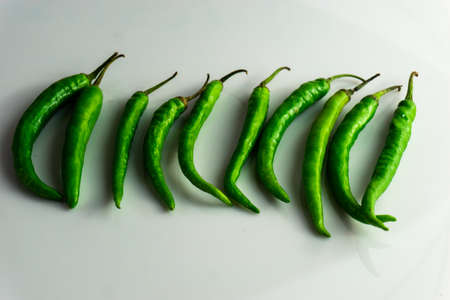 Group of green chilly stacked together on a white background