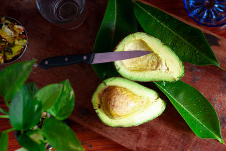 Avocado cut into two pieces with a knife placed on a wooden backgroundの写真素材