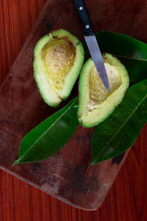 Avocado cut into two pieces with a knife placed on a wooden backgroundの写真素材