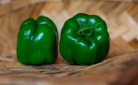 Fresh green capsicum vegetable placed on a bamboo background