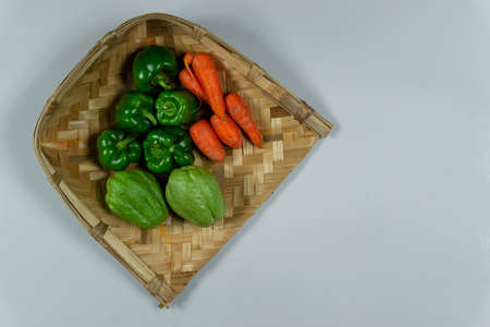 Fresh raw vegetables stacked in a bamboo Pan placed on a white background with copy space