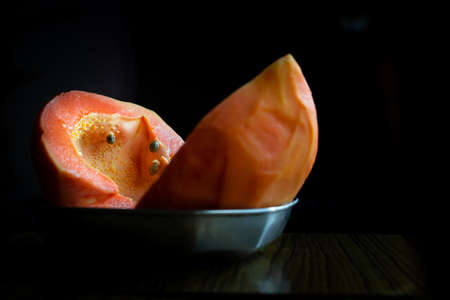 Fresh Papaya fruit cut into two pieces kept in a plate on a wooden table with selective focus
