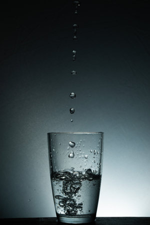 Water drops into a half glass of water in it with selective focusの写真素材