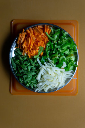 Fresh Cut carrot potato capsicum and beans vegetables stacked together in a plate
