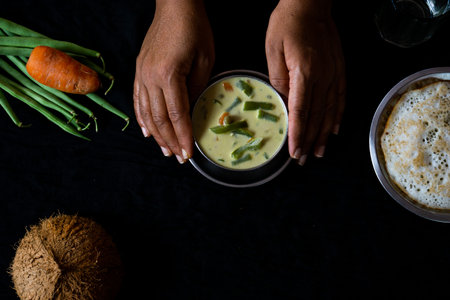 Human hands holding delicious homemade vegetable stew in a bowl on a black backgroundの写真素材