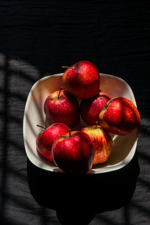 A bunch of healthy apples stacked together in a bowl with dark background and artistic lightingの写真素材