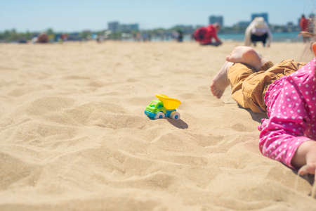 Kid's hand playing with a toy truck in the sand on the beachの写真素材
