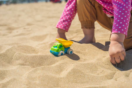 Kid's hand playing with a toy truck in the sand on the beachの写真素材