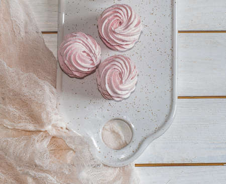 pink homemade marshmallow (zephyr) lies on a white plate on a wooden table. Top view