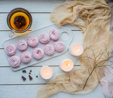 pink handmade marshmallows, marshmallows on a light wooden table, hot tea in a glass mug and next to...