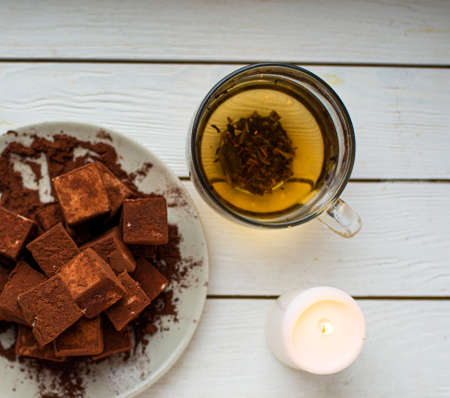 handmade souffle cubes covered with cocoa powder lie on a plate on a light wooden table, hot tea in...