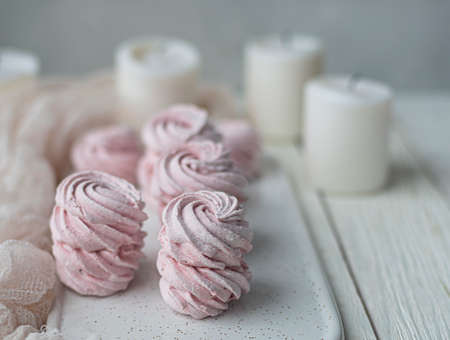 homemade Marshmallow zephyr with candles on a white plate on a light wooden table. Pink sweet...